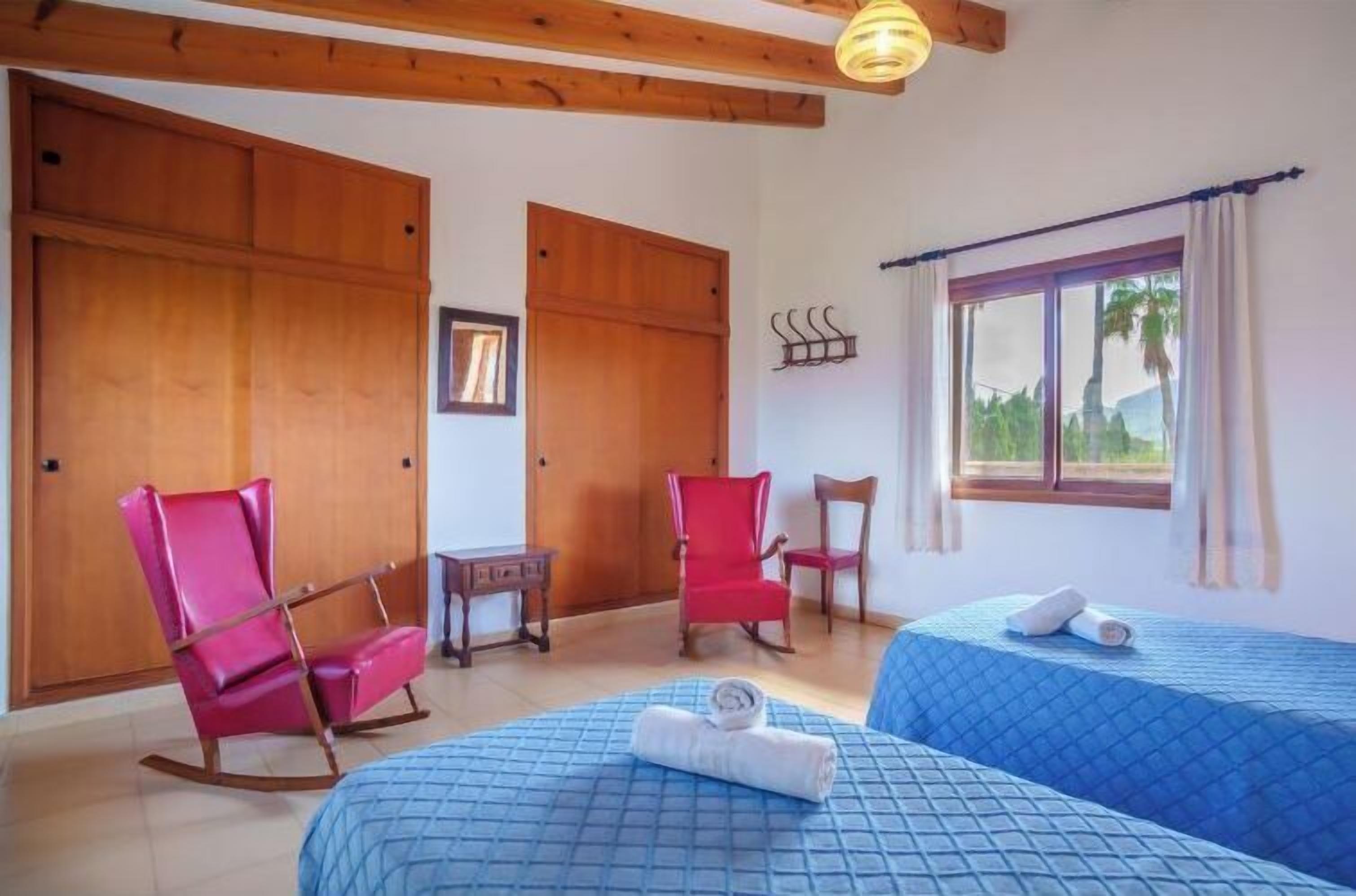Una habitación con dos camas, muebles de madera, un ventanal con cortinas y vistas al exterior con vegetación.