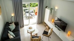 Una sala de estar moderna con un sofá, dos sillones de mimbre, una pequeña mesa redonda, un televisor y un balcón con puerta corrediza.