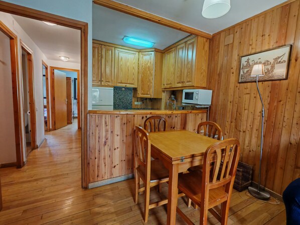 Una cocina con paneles de madera, una mesa de comedor con sillas, un microondas y un cuadro en la pared.