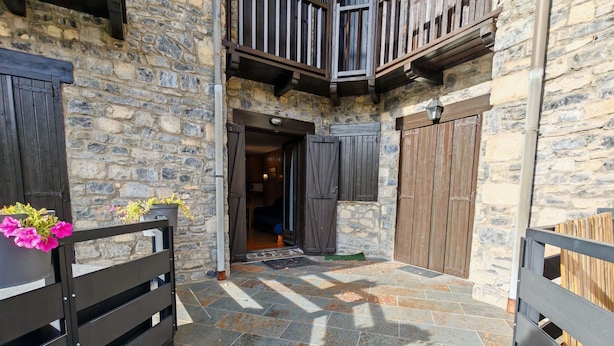 A stone building with a wooden balcony, a tiled patio, and a wooden gate.