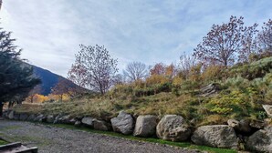 A gravel path with a stone wall and grass on one side, and a hill with trees and shrubs on the other.