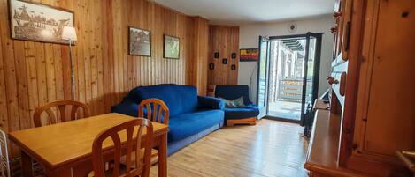Une pièce aux murs lambrés, comprenant une table à manger, des chaises, un canapé bleu et un buffet en bois.