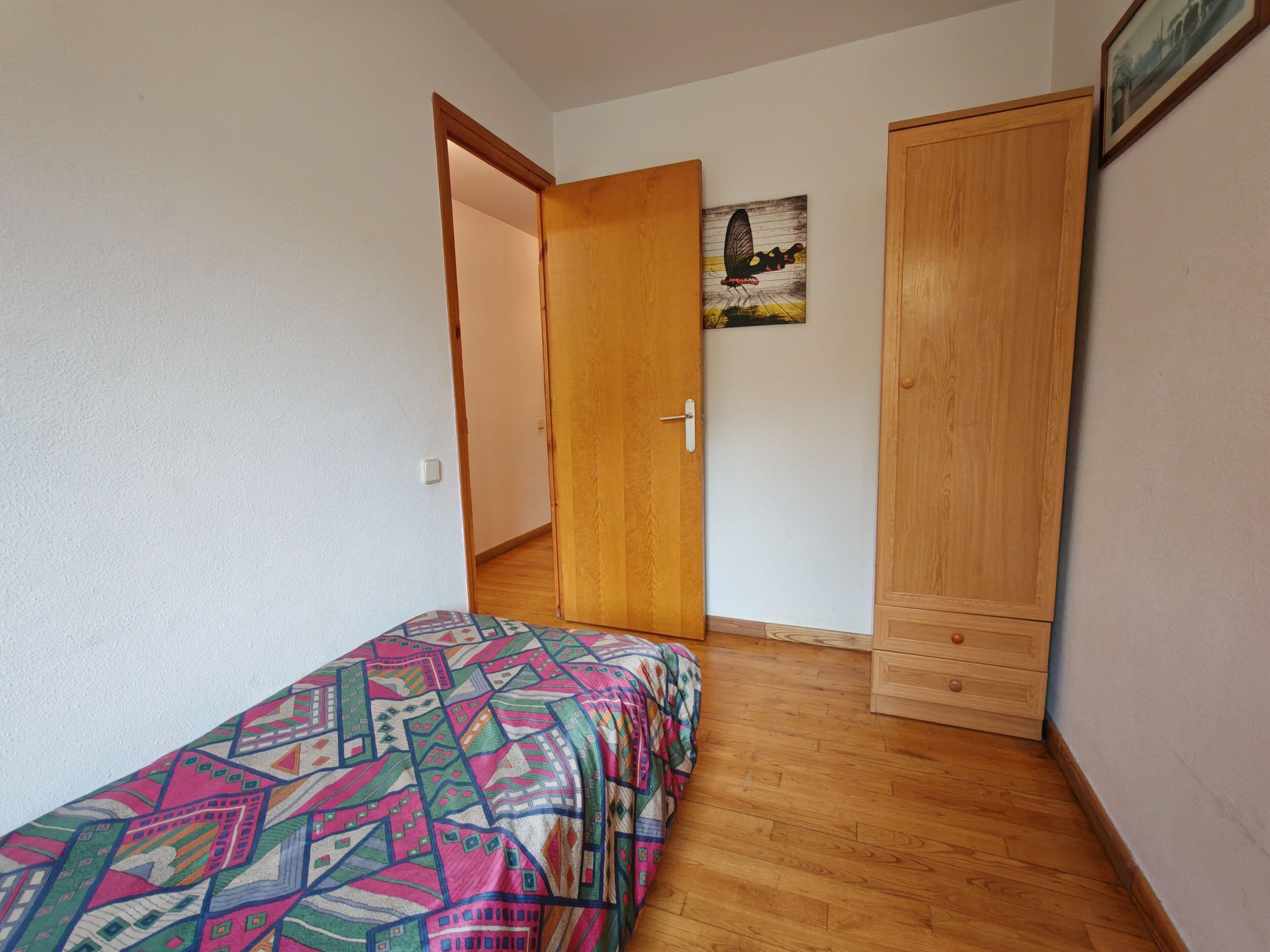 A bedroom with a bed, a wardrobe, and a door leading to another room.