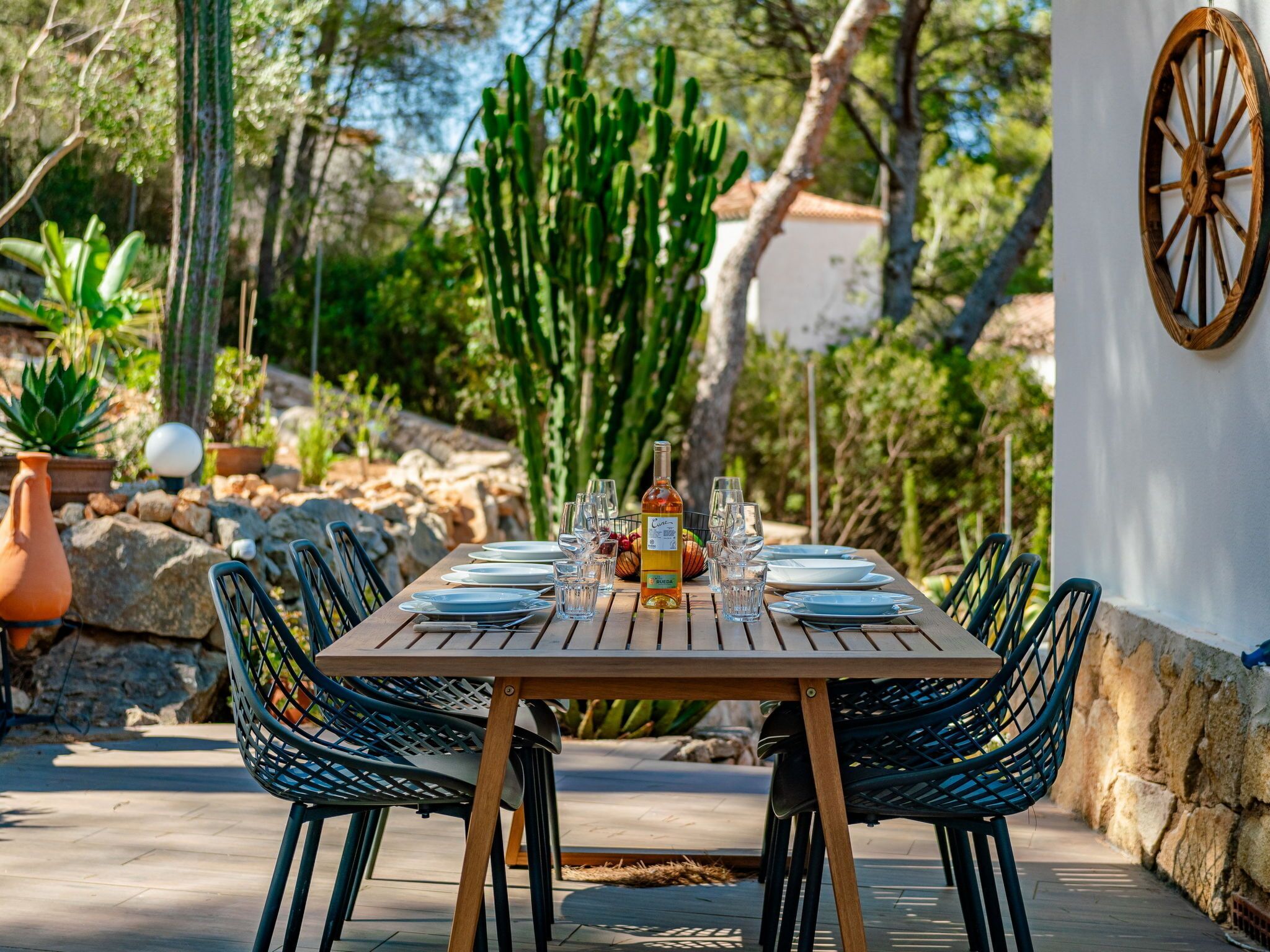An outdoor dining area with a wooden table set for six, surrounded by wicker chairs.