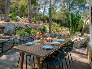 Een terras met een houten tafel voor vier personen, omringd door stenen muren en verschillende planten.
