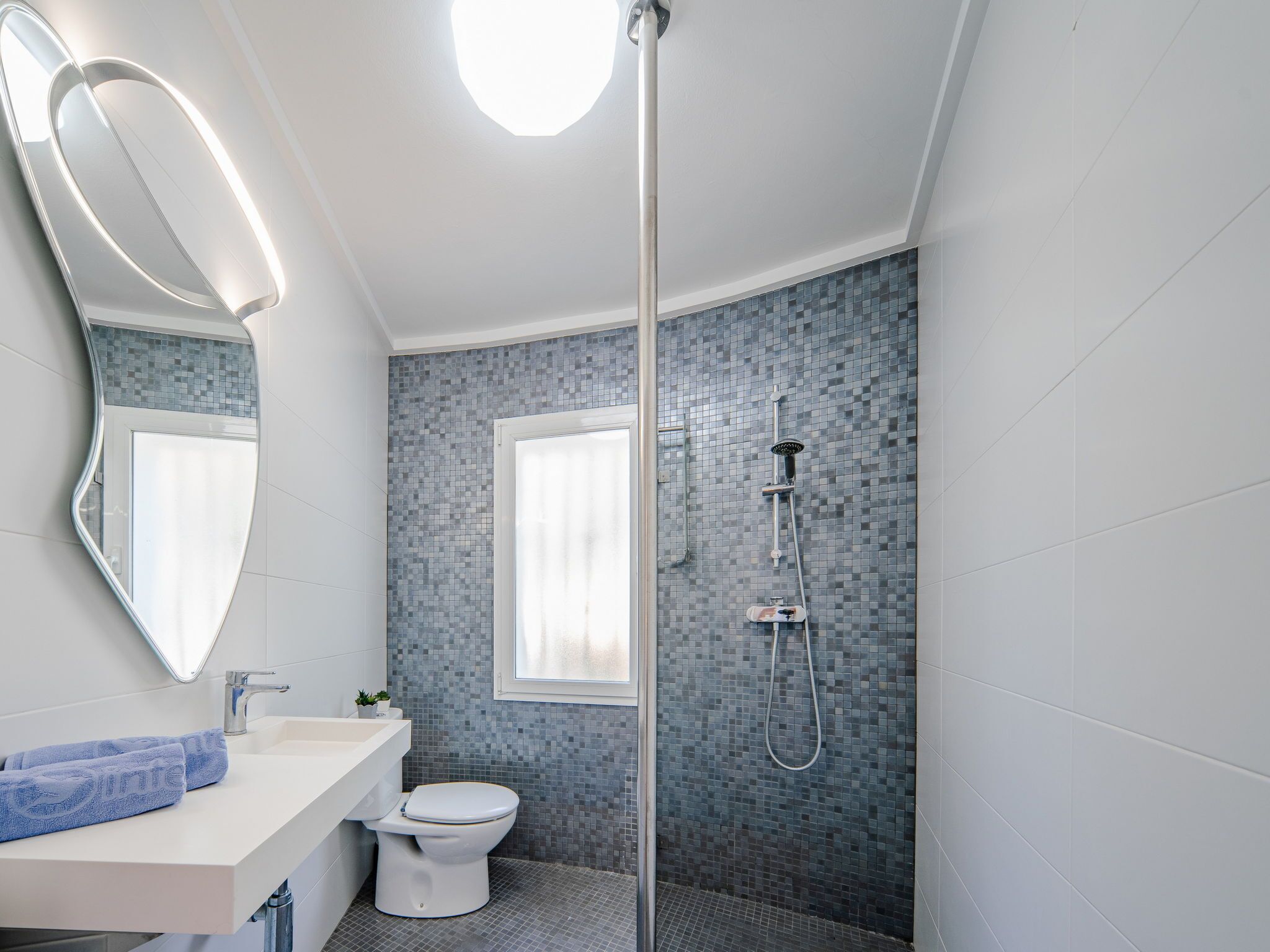 Une salle de bain moderne avec un lavabo, des toilettes et une douche, le tout de couleur blanche.