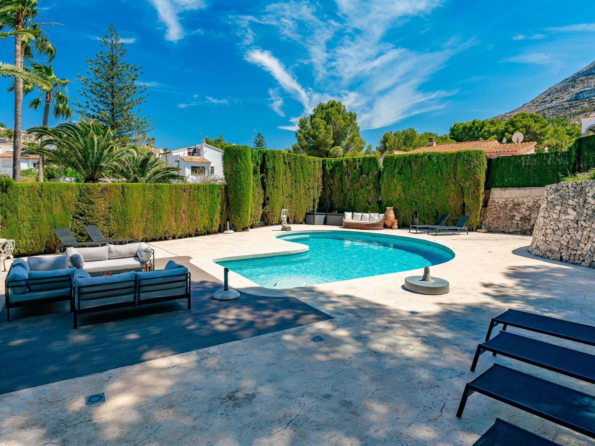 A pool area with a curved pool, lounge chairs, and a stone wall.