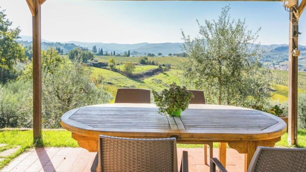 Une pergola en bois installée à l’extérieur, avec une table et des chaises, offrant une vue panoramique sur un paysage pittoresque composé de collines et d’arbres.