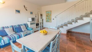 A living room with a sofa, a dining table with chairs, a kitchen area with a microwave, and a staircase.