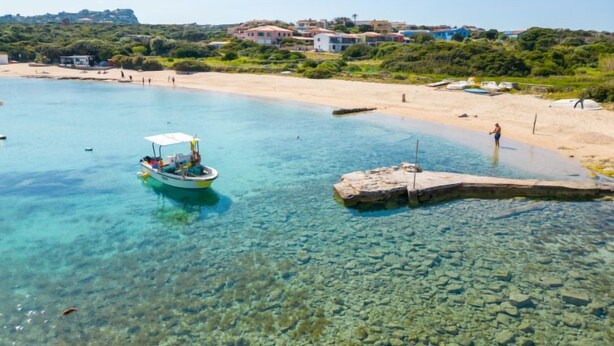 A coastal scene with clear turquoise waters, a boat, and a rocky outcrop.