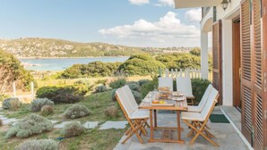 A patio with a table and chairs overlooking a scenic view of a beach and hills.