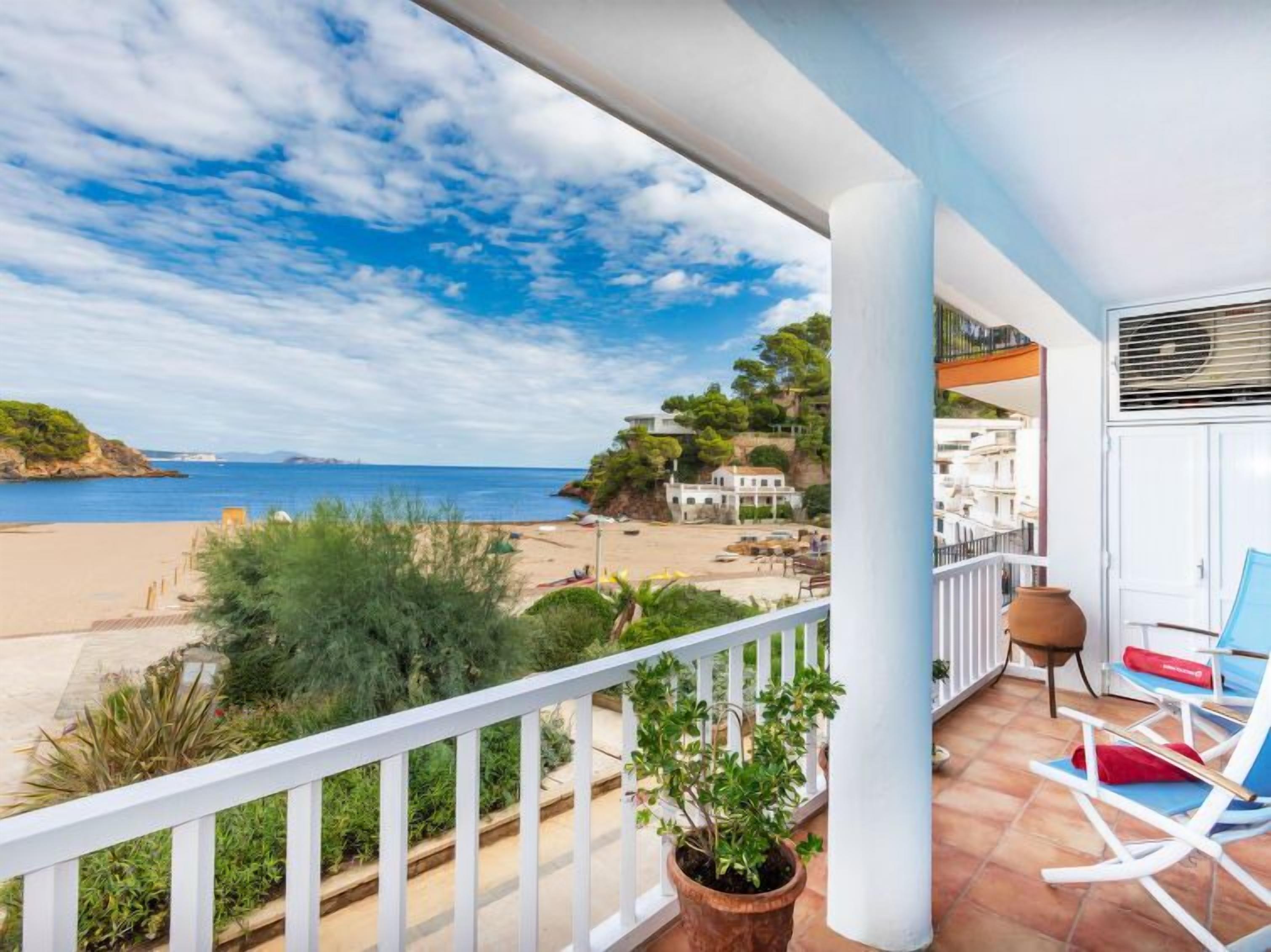 A balcony with a view of the beach and ocean, a potted plant, and a seating area with a chair and a table.