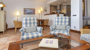 A living room with two checkered armchairs, a glass coffee table, a wicker chair, and a painting on the wall. - Sa Riera Beach by Interhome (Begur)