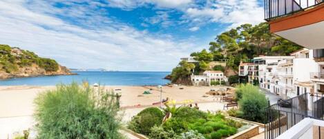A coastal view with a beach, greenery, and buildings.