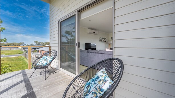 Ein Balkon mit zwei Stühlen, einem Sofa, einer Schiebetür und Blick auf den Garten.