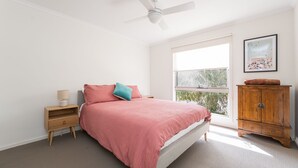Ein Schlafzimmer mit einem Bett, einem Nachttisch, einem Holzschrank, einem Deckenventilator und einem Fenster mit Blick.