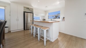 Eine moderne Küche mit weißen Schränken, einem Edelstahlkühlschrank, einer Holz Arbeitsplatte und drei Barhocker.
