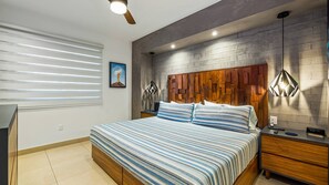 Quarto com cama, mesas de cabeceira, cabeceira de madeira, ventoinha no teto e luminária na parede.