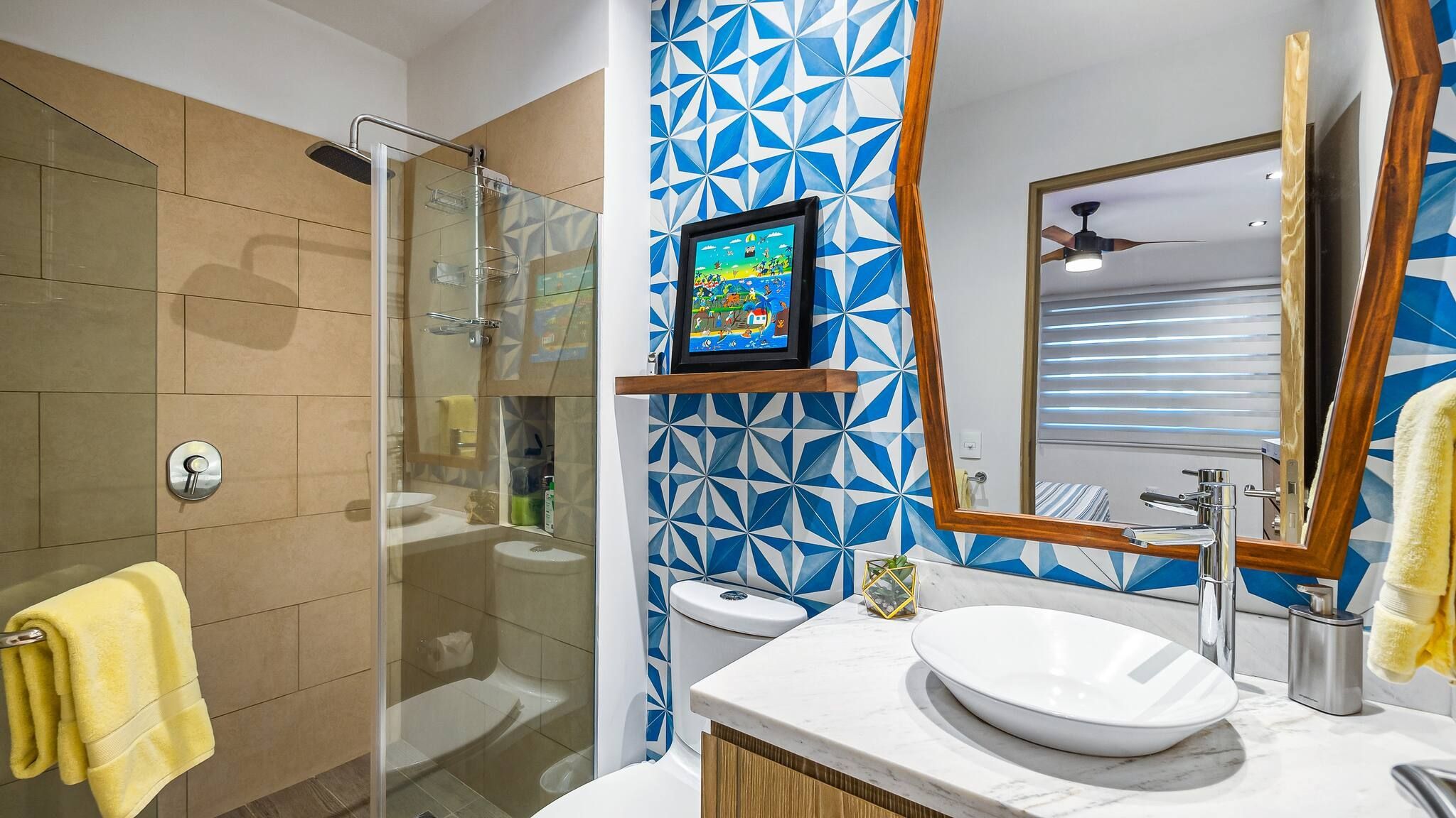 Een moderne badkamer met een glazen douchecabine, een wit wastafeltje en een wand met een blauw geometrisch patroon.