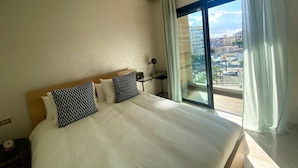 Ein Hotelzimmer mit einem großen Bett, einem Schreibtisch und Blick auf die Stadt durch ein großes Fenster.