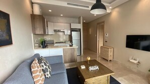 Ein modernes Wohnzimmer mit einem grauen Sofa, einem Holztisch und einer Küche im Hintergrund.