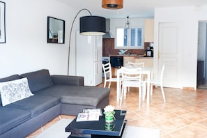 A modern living room with a grey sofa, a black coffee table, and a white dining area with chairs.
