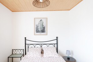 A bedroom with a bed, a bedside table, a lamp, a framed picture on the wall, and a ceiling fan.
