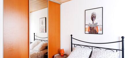 A bedroom with a bed, a nightstand, a lamp, a wall art piece, and a wooden wardrobe.