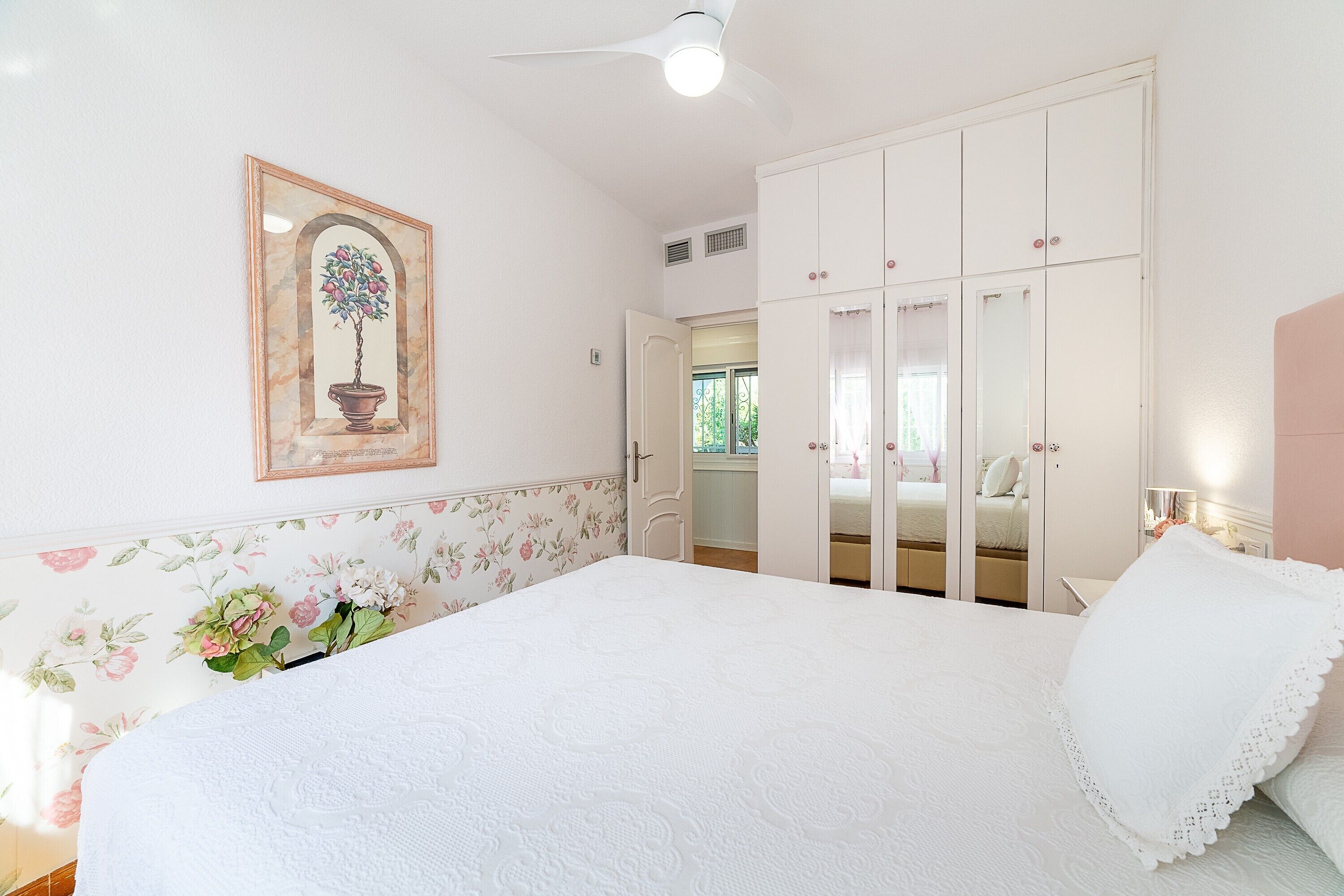 Une chambre à coucher comprenant un lit, une armoire, un ventilateur de plafond et un papier peint à motifs floraux.