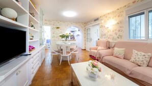 A living room with a TV, white furniture, a pink sofa, and a dining area with a table and chairs. - Holiday Home "Cortijo Indalo" with Pool & Wi-Fi (Pechina)