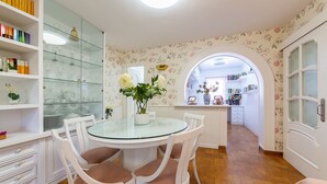 A dining area with a glass-top table, white chairs, a white cabinet with glass doors, and a floral wallpapered wall. - Holiday Home "Cortijo Indalo" with Pool & Wi-Fi (Pechina)