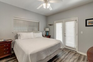 A bedroom with a bed, a nightstand, a dresser, a ceiling fan, and a door with blinds. - Just a short walk to the pristine sandy beaches! Take a stroll on the beach, bui (Port Aransas)