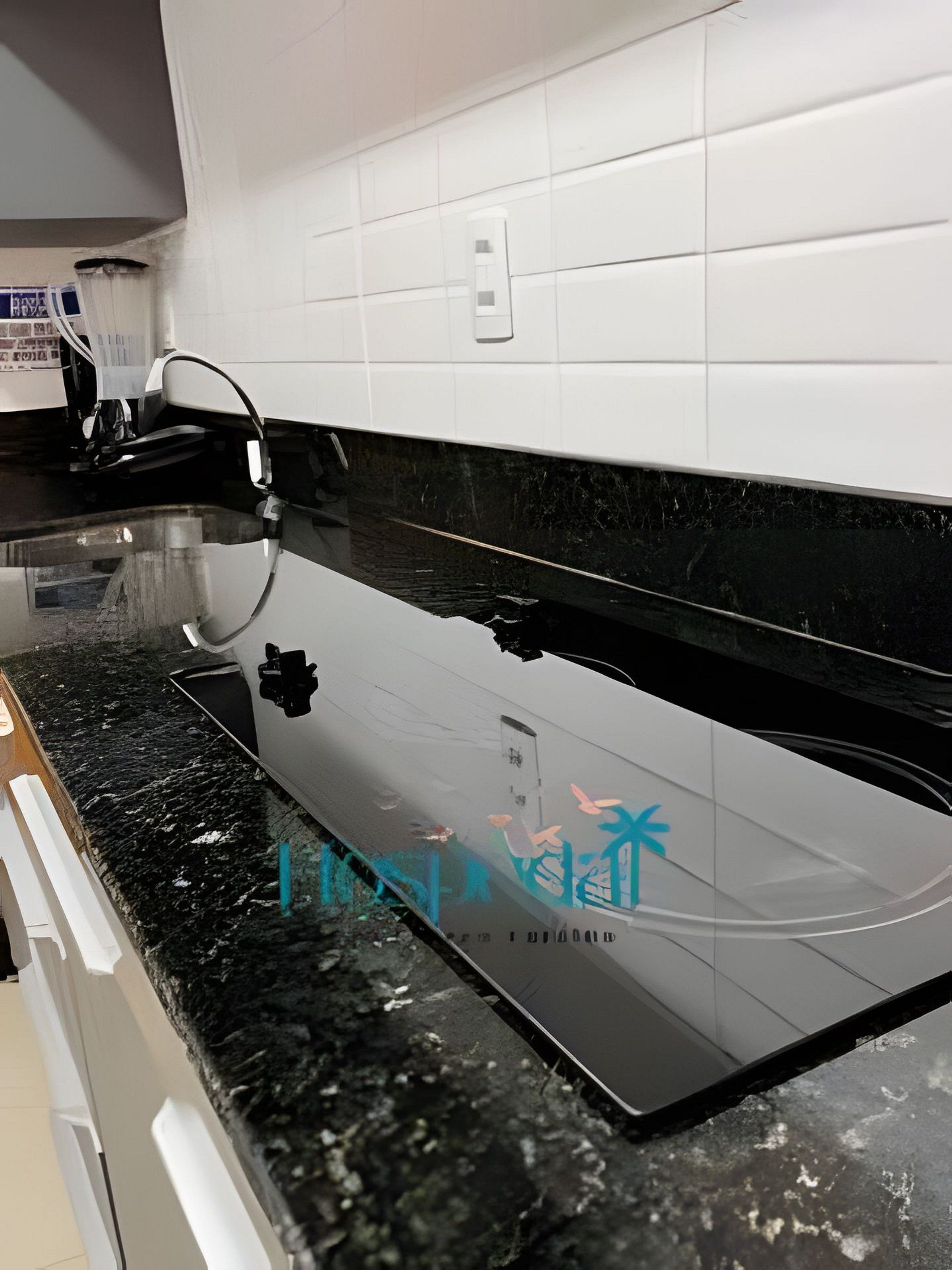 A kitchen with a black countertop, white tiled backsplash, and a stainless steel range hood.