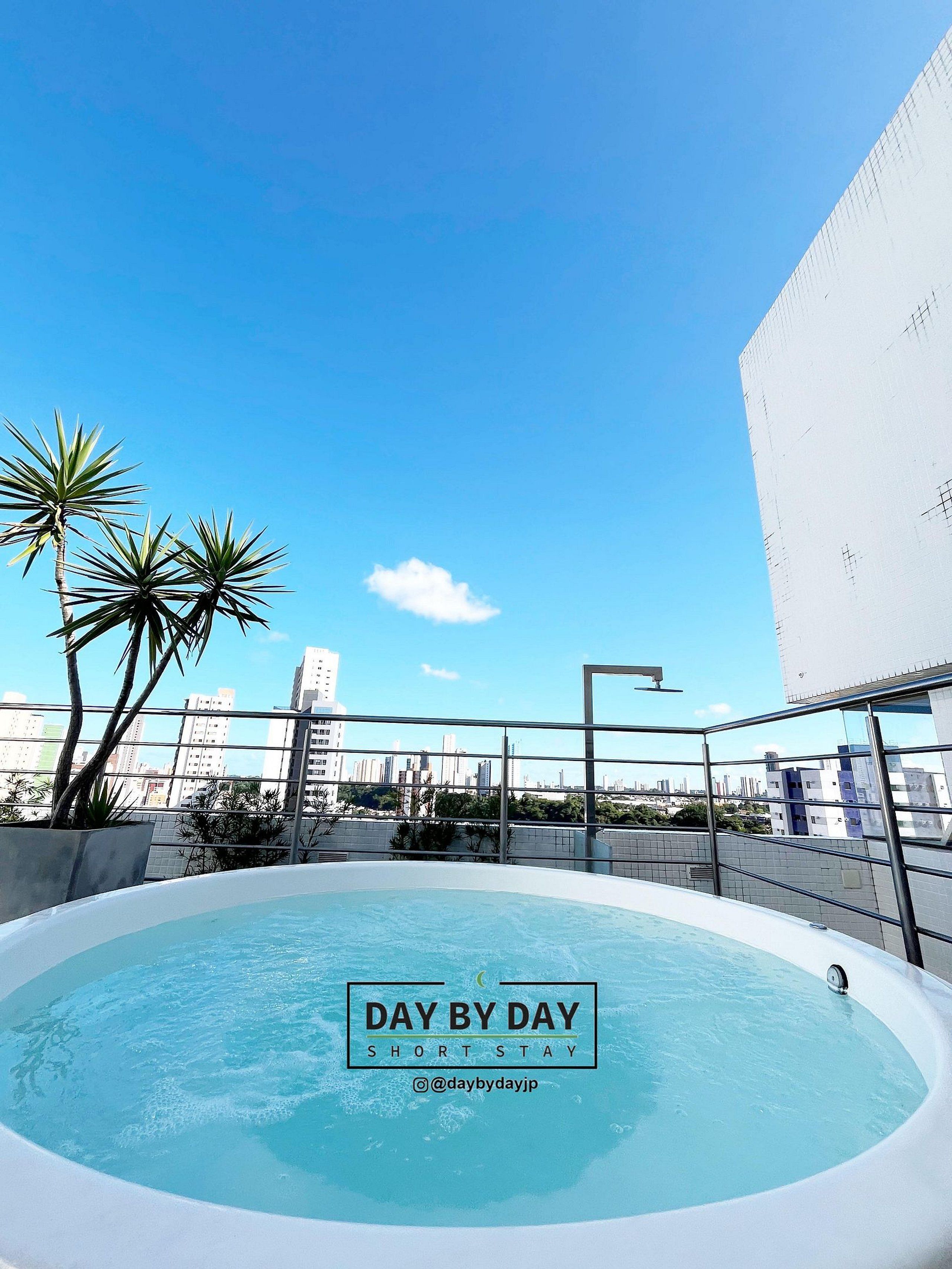 Piscina no terraço com céu azul límpido, cercada por edifícios e palmeiras.