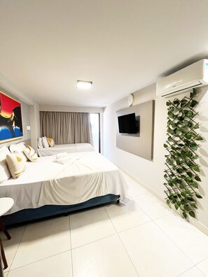 Una habitación de hotel con una cama, un televisor de pantalla plana, un equipo de aire acondicionado y una planta en la pared.