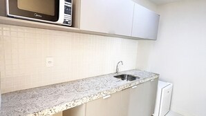 A kitchen with a microwave, sink, and cabinets. - Manaira Apart Hotel (João Pessoa)