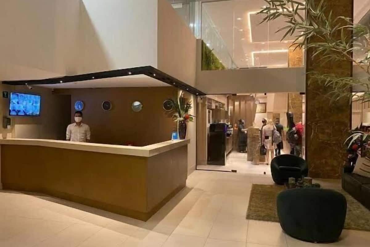 A hotel reception area with a reception desk, a TV screen, and a large potted plant.