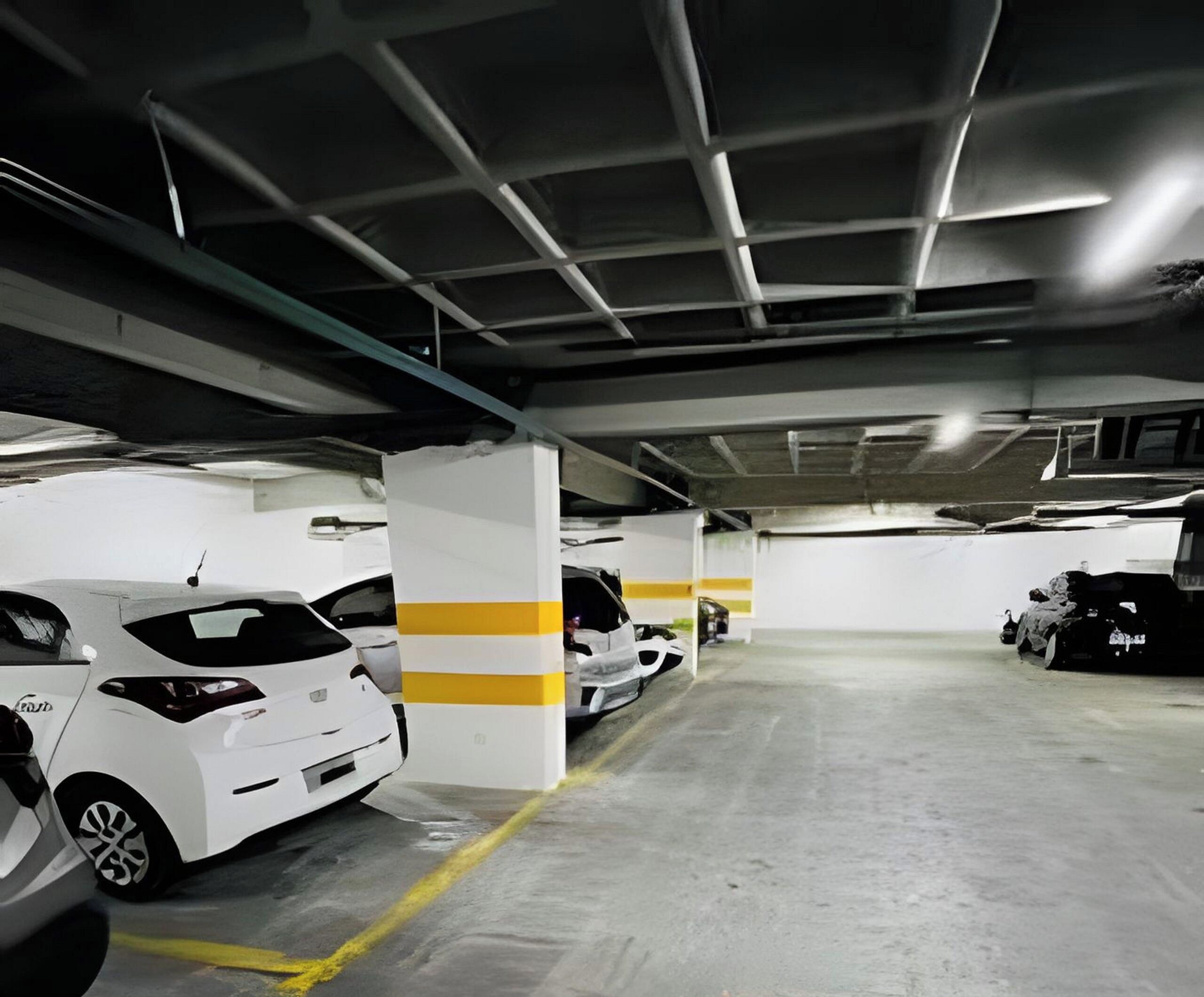 Un parking avec plusieurs voitures blanches stationnées dans des emplacements prévus à cet effet, des piliers en béton et un éclairage au plafond.