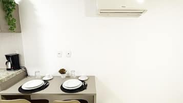 Een moderne eetruimte met een tafel gedekt voor twee personen, een koffiezetapparaat en een airconditioner aan de muur.