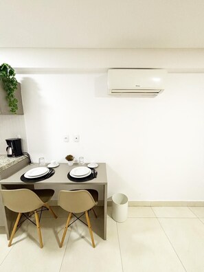 Un moderno comedor con una mesa preparada para dos personas, una cafetera y un aire acondicionado en la pared.