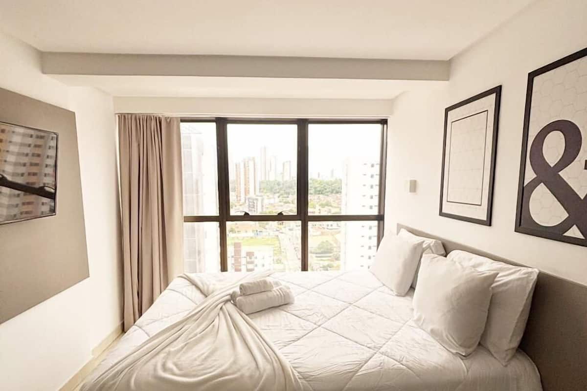 A bedroom with a large window, a bed, and a city view.