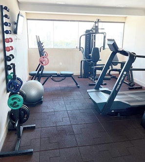 Un gimnasio con equipo de ejercicio, una banca y un ventanal grande.