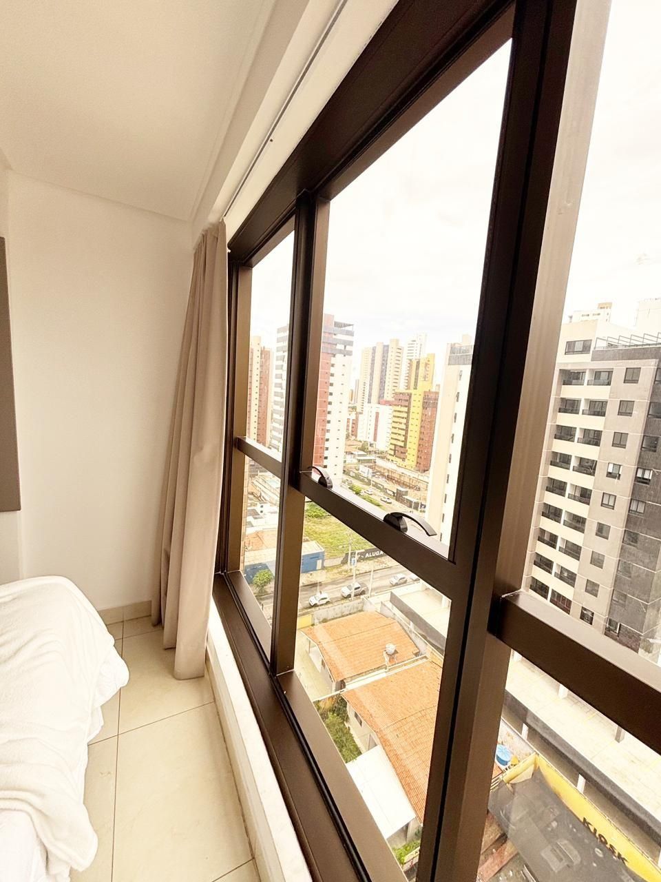 A hotel room with a large window, a bed, and a view of the cityscape.
