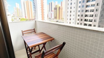 A balcony with a wooden table and chairs, a tiled floor, and a view of high-rise buildings.