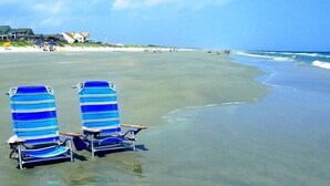 A beach with two striped beach chairs and a bench, a clear sky, and a calm sea.