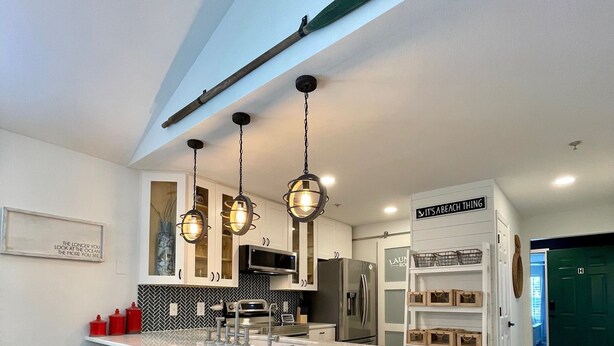 A modern kitchen with a central island, black bar stools, pendant lighting, and a view of the living area.