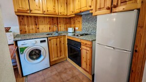 Eine kompakte Küche mit Holzausstattung, einer Waschmaschine, einem Geschirrspüler und einem Kühlschrank.