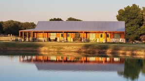 A wooden building with a metal roof, reflecting in a calm body of water. - Private Retreat with Pond, Pool and Hot Tub (Boyd)