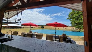 An outdoor bar area with a pool view, red umbrellas, and outdoor seating. - Private Retreat with Pond, Pool and Hot Tub (Boyd)