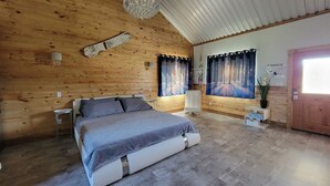 A bedroom with a large bed, wooden walls, a chandelier, curtains, and a door. - Private Retreat with Pond, Pool and Hot Tub (Boyd)